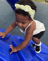 Little girl is wearing a baby headband featuring a checkered print from By Bella Boutique.